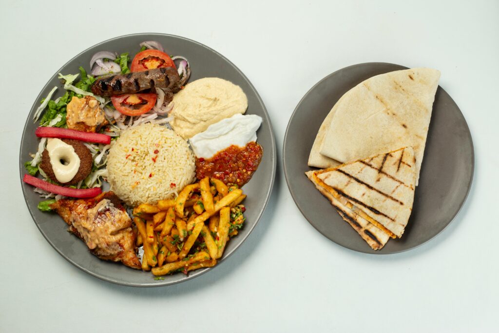 A vibrant flat lay of a Middle Eastern meal with rice, hummus, sausage, and pita bread.